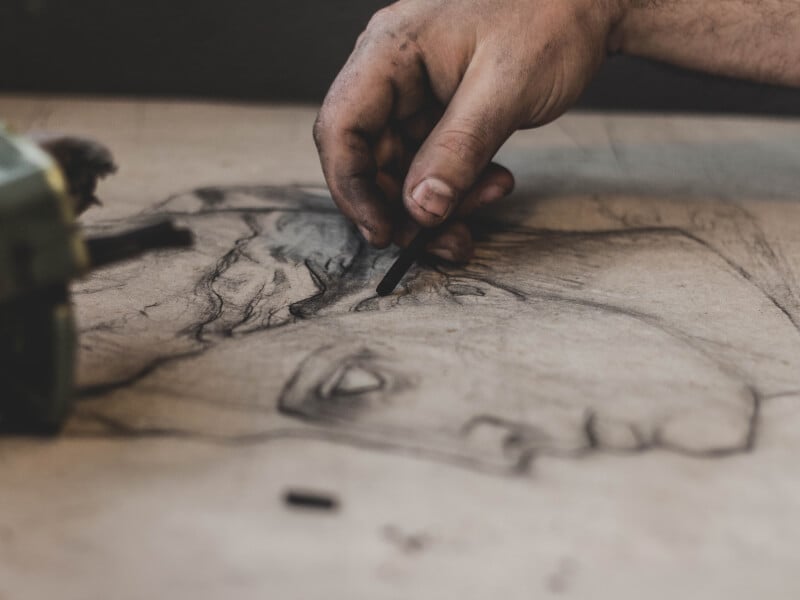 A stained hand draws a portrait in charcoal